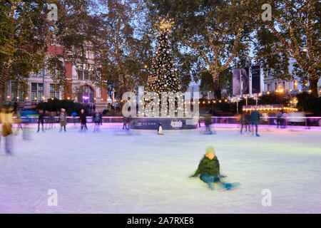 Movement Blur image of people skating on Christmas decorated Ice Rink at the London Natural History Museum at Dusk, around the central xmas tree. Stock Photo