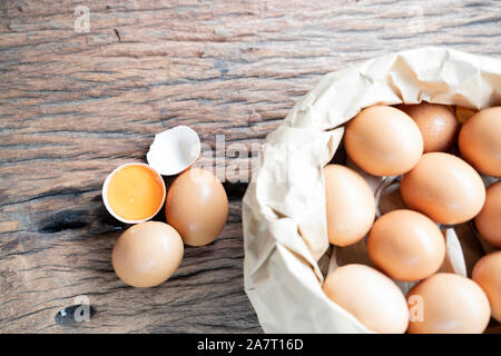 Broken eggs containing and egg yolks on table wooden floors and eggs in brown bag. Stock Photo