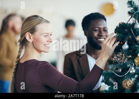 Portrait of beautiful young woman looking at decorations on Christmas tree during party banquet, copy space Stock Photo