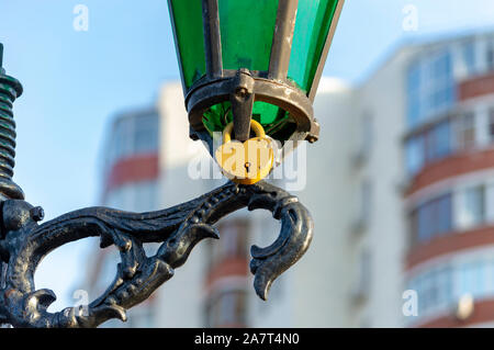 Yellow metal padlock on lamppost in park in honor of  love of girl and guy. View from below. Stock Photo