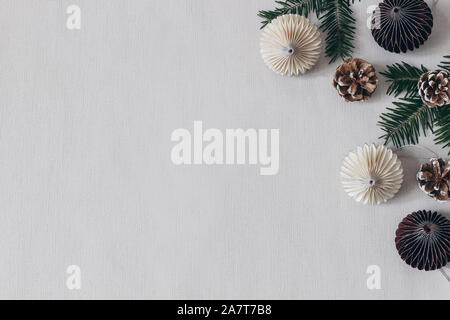 Christmas styled stock composition. Decorative paper Christmas ornaments, pine cones and fir tree branches on grey table linen background. Flat lay, t Stock Photo