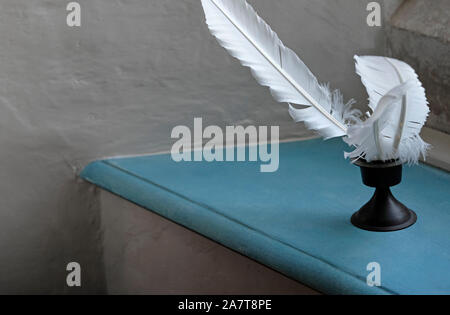 white feather quills in inkwell on blue painted shelf Stock Photo