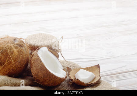 Coconut shell with meat on hemp sackcloth on white wooden kitchen table Stock Photo