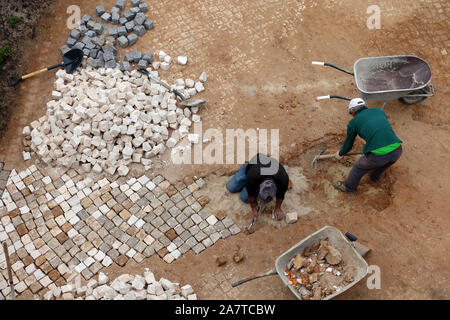 Sagres, Portugal 15 April 2019: Looking down on two men building a paved area using the traditional Calcada method which Portugal is famous for. Stock Photo