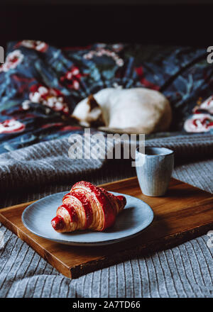 Cherry croissant with a cup of espresso on a wooden tray in a bed. The concept of cozy morning at home. Stock Photo