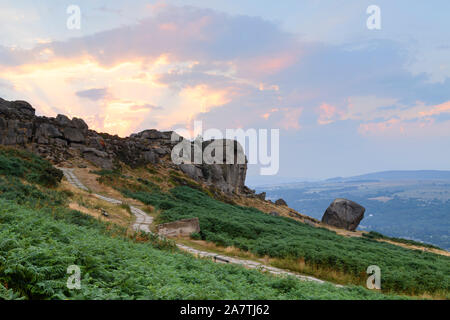 Rural scenic landscape (dramatic colourful sunset sky, sun rays, high rocky outcrop, valley) - Cow & Calf Rocks, Ilkley Moor, Yorkshire, England, UK. Stock Photo