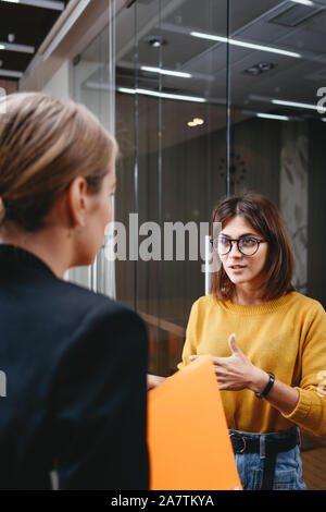 Team of handsome business women have meeting at modern office. Two positive female employees standing at open space and discuss working moment Stock Photo