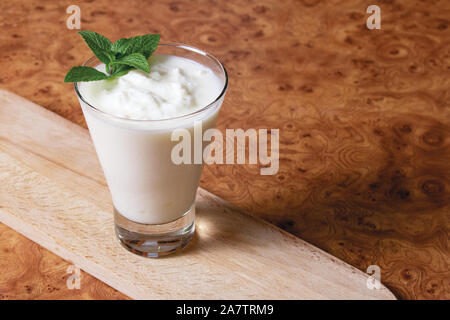 Kefir in a glass goblet with a mint branch on a wooden board on a brown background Stock Photo
