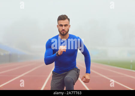 The guy the athlete does squats in the stadium in the fog Stock Photo