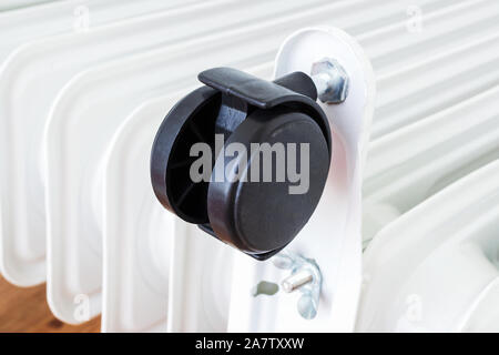 Close-up of a plastic twin wheel on an electric oil heater. White oil-filled radiator with four black wheels. Home heating and comfort. Stock Photo