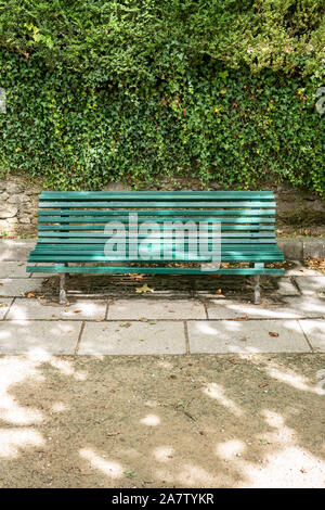 Green wooden bench with a decorative ornate metal legs and armrests on public park. Galicia, Spain Stock Photo