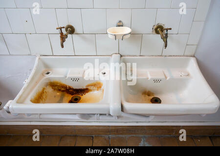 Two dirty sinks / wash basins covered in rusty stains in bathroom of disused clinic Stock Photo