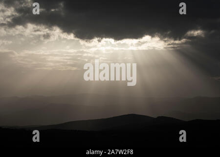 The sun is hidden behind the cloud on a grey landscape and mountains Stock Photo