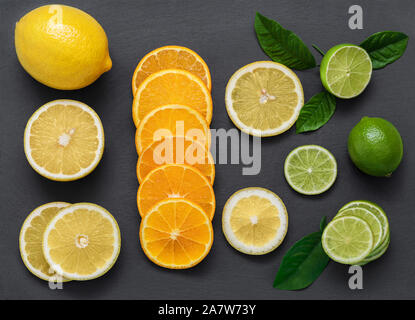 Sliced citrus fruit on a stone table. Juicy ripe slices of orange, lemon and lime on a black background. Fruit mix, top view closeup. Stock Photo