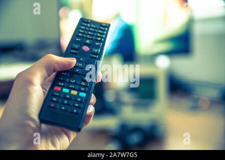 TV remote control in the foreground, tv in the blurry background. Stock Photo