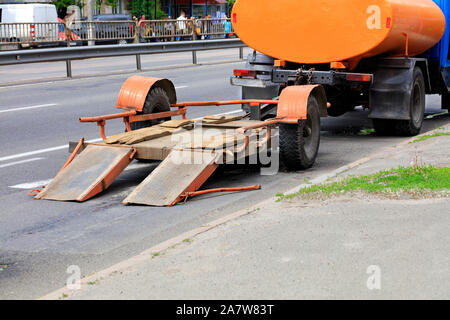 An old low-platform trailer hitched to an old truck that stands on a roadway. Stock Photo