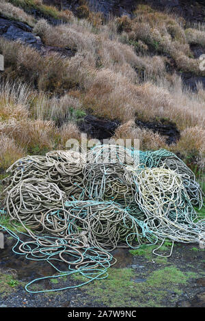Pile of fishermen’s ropes coiled on the harbour with wet rocks and grasses in the background on a rainy day. Stock Photo