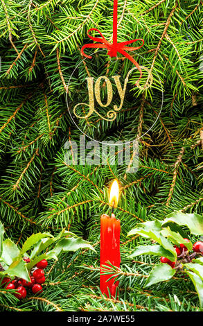 Joy Holiday Ornament Over Candle on Evergreens and Holly Stock Photo