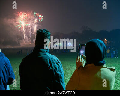 A young Asian couple at a public fireworks display, recording the fireworks on a mobile phone Stock Photo