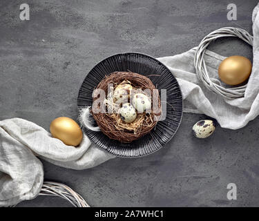 Easter flat lay on dark background with golden painted eggs in the nest, linen textile and quail eggs on dark textured background. Conscious consumpti Stock Photo