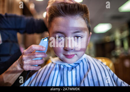 Mixed race Asian Caucasian boy wearing a stripped apron getting a flat top flattop haircut with a razor Stock Photo