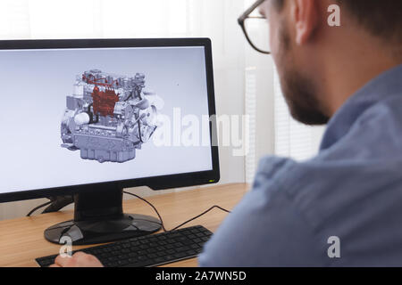 Engineer, Constructor, Designer in Glasses Working on a Personal Computer. He is Creating, Designinga New 3D Model of Car Engine, Motor in CAD Program Stock Photo