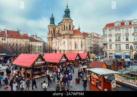 People walking among wooden kiosks offering souvenirs and traditional food during Christmas market in Prague. Stock Photo