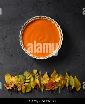Thanksgiving or harvest concept. Bright orange pumpkin pie and colored leaves looking like sunset over woods on black background copy space Stock Photo