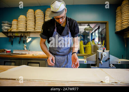 A professional baker works on a long sheet of pastry dough in kitchen Stock Photo