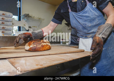 Close-up view of a baker placing hot loaf of bread on countertop Stock Photo