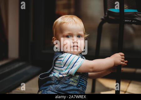 Sitting baby boy holding chair leg looking worried or startled Stock Photo