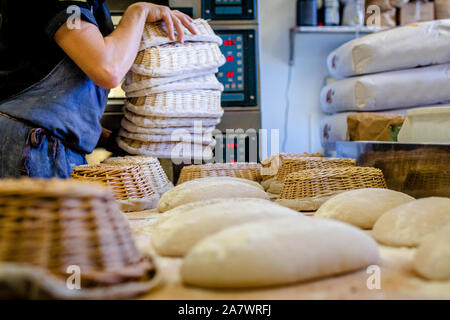 A professional baker with a stack of baskets places bread on counter Stock Photo