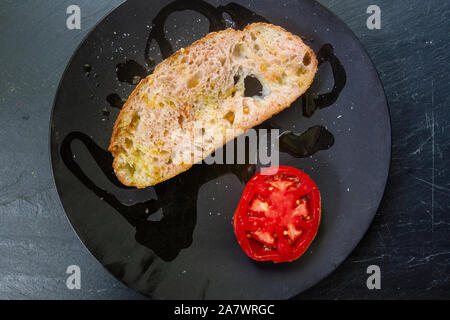 Fresh-baked bread slice  on a black  plate with olive oil and tomato Stock Photo