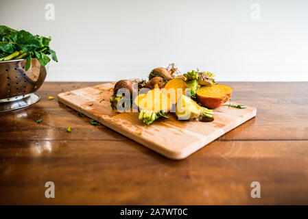 freshly chopped beets on cutting board next to colander full of greens Stock Photo