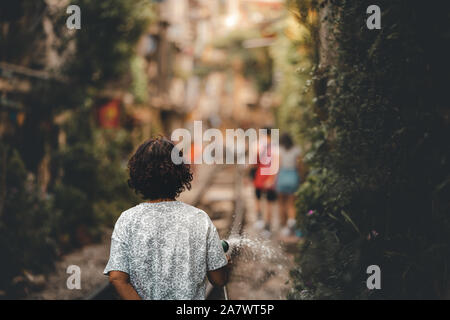 A local woman living on the world famous Train Street in Hanoi, Vietnam waters the plants and her garden as tourists walk by Stock Photo