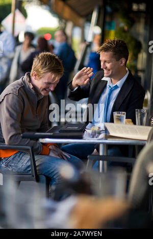Young homosexual couple laughing while sitting at a cafe table. Stock Photo