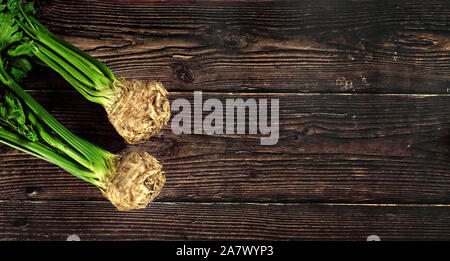 Celeriac root bulbs with green leaves on dark wooden board. Wide banner, space for text right side Stock Photo