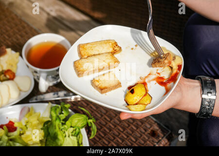 Woman hand holding fork and plate with grilled potatoes, and tofu soy bean curd with ketchup and mustard - vegetarian barbecue grilling Stock Photo