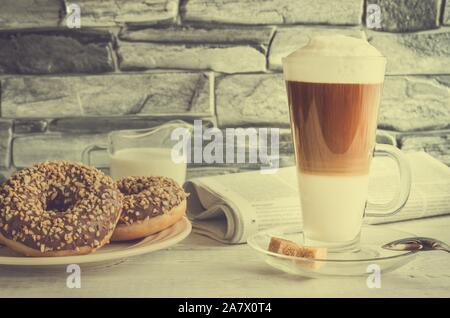 Conceptual delicious sweet breakfast in vintage style. Latte macchiato coffee  with sweet donuts with a hole and morning newspaper. Stock Photo