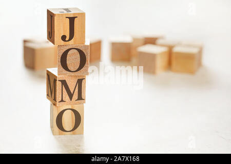 Four wooden cubes arranged in stack with text JOMO meaning Joy of missing out on them, space for text image at down right corner Stock Photo