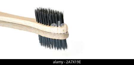 Wooden bamboo toothbrush with black bristles, closeup detail isolated on glossy white table reflection visible , space for text right side Stock Photo