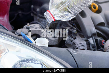 Pouring distilled water ecological alternative to washing fluid to washer tank in car, detail on liquid flow from clean plastic bottle Stock Photo