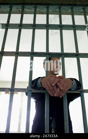 Confident young businessman standing in a empty prison cell behind bars in a derelict building. Stock Photo