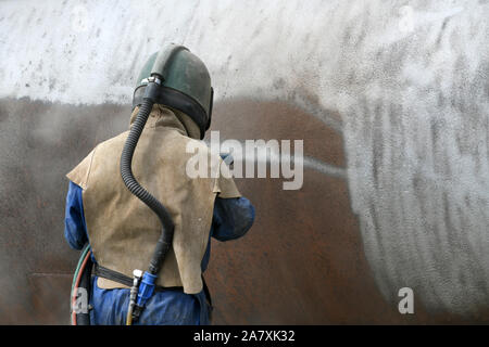 A man weating full safety gear uses ground glass to sandblast the steel casing of a meat drying machine for a rendering plant. (Focus on the surface b Stock Photo