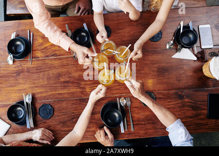 Big family toasting with mugs of tasty sweet fruit cocktail when sitting at cafe table, view from the top Stock Photo