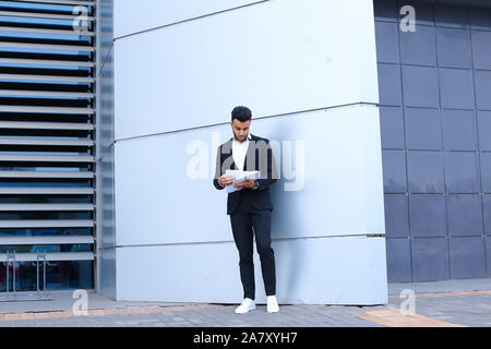 Arabian entrepreneur man holds and considers, reads documents, stands in full growth near wall of business center. Stock Photo