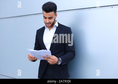 Arabian Successful businessman holds documents, smiling little smile and thinks near wall of business center. Stock Photo