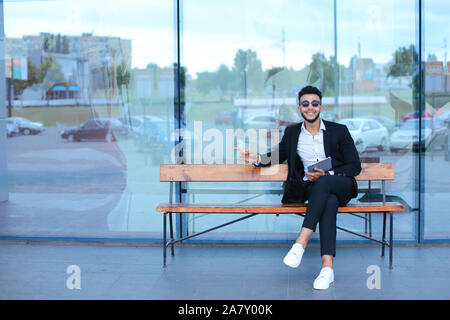 Man in suit arabic puts on sunglasses with tablet near business center Stock Photo