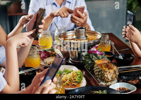 Hands of party guests sitting at dinner table with traditional Asian cuisine and texting friends of checking social media on smartphones Stock Photo