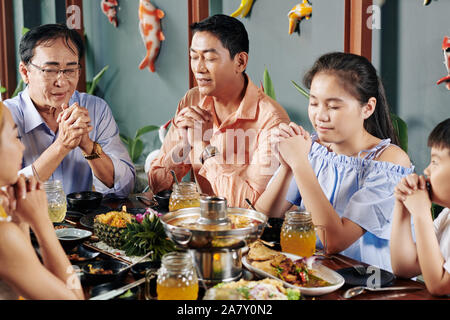 Vietnamese family members closing eyes when praying before having dinner at home Stock Photo